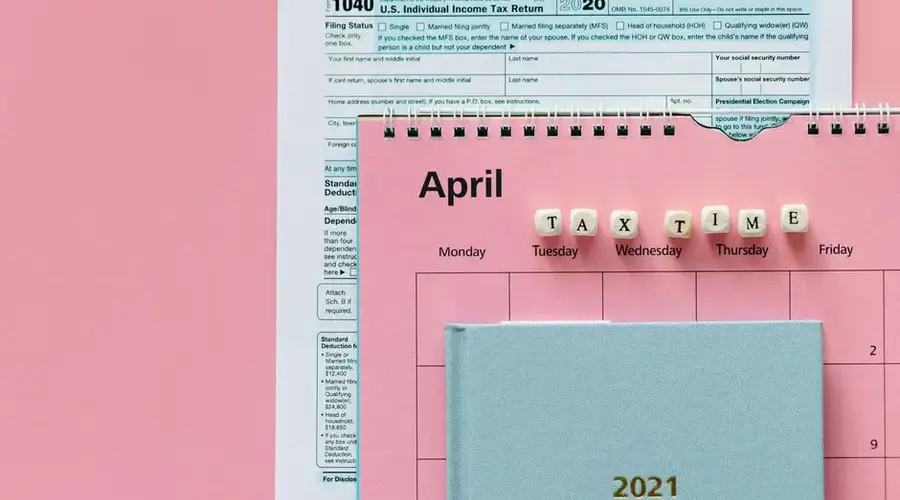 Flat lay image of tax forms, calendar, and 'tax time' reminder on a pink background.