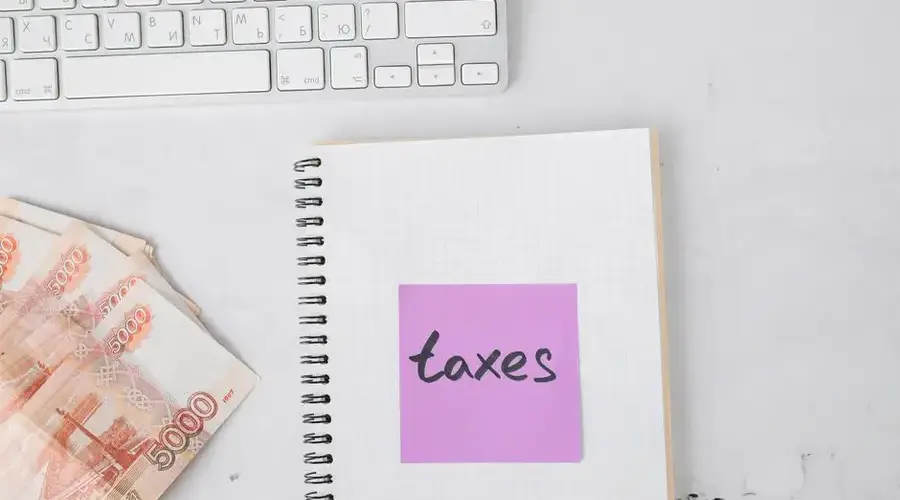 Close-up of a notebook with 'taxes' sticky note, currency bills, and a keyboard symbolizing financial planning.