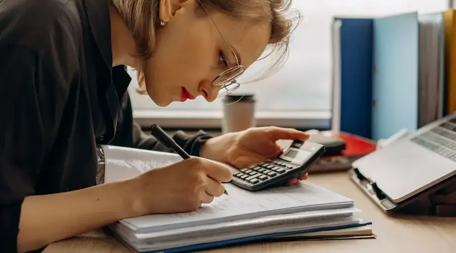 Young woman diligently working on accounting with a calculator and documents. Perfect for business and finance themes.