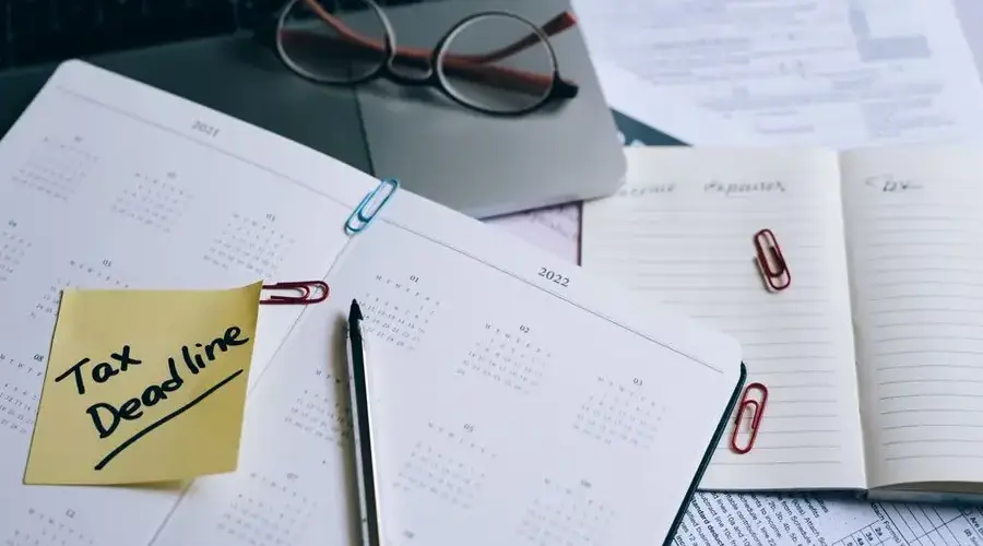 A desk with a planner, sticky note marked 'Tax Deadline', and paperwork, indicating financial planning.