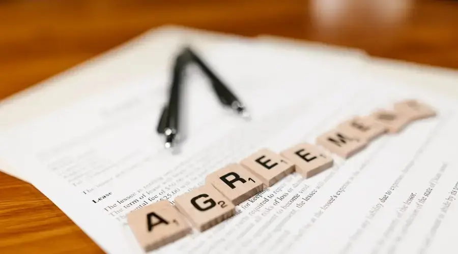 Scrabble tiles spelling 'AGREEMENT' on a lease document, emphasizing contractual themes.