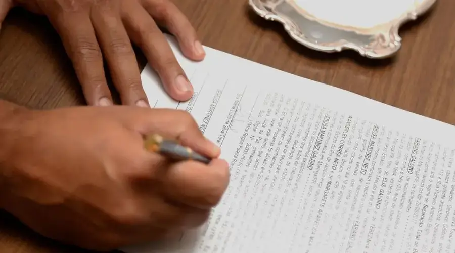 Hand signing a contract on a wooden desk, emphasizing business formalities.