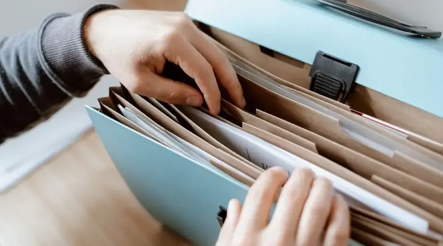 Crop unrecognizable person selecting document in opened briefcase for documents placed on wooden table