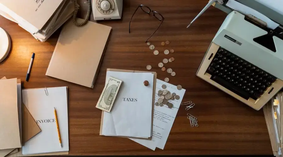 Retro office scene featuring a typewriter, coins, documents, and stationary on a wooden desk.