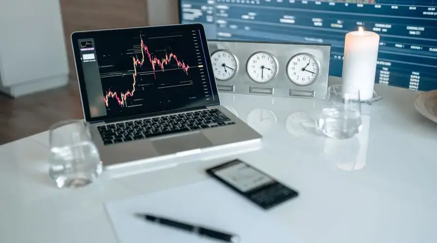 A contemporary workspace featuring a laptop, candle, and clocks on a white desk, ideal for finance and technology themes.