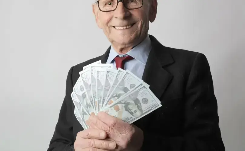 Senior man in a suit with glasses holding US dollars, symbolizing wealth and savings.