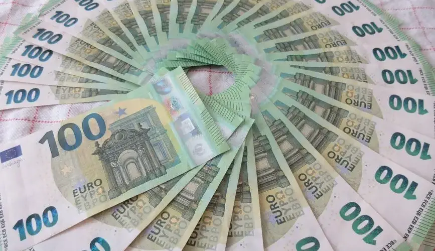 Close-up of a fan of 100 euro banknotes arranged in an artistic circle pattern on a textile surface.