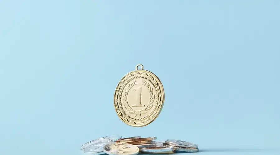 A gold medal and pile of coins on a light blue background representing achievement and savings.