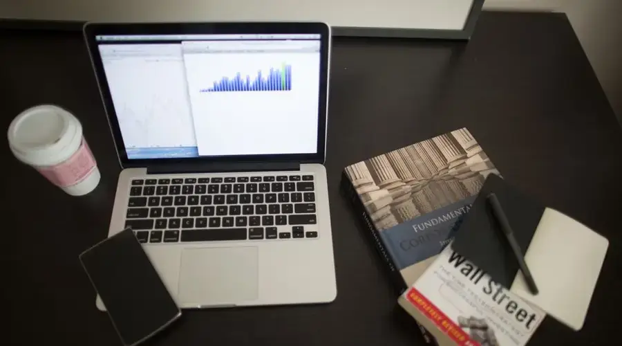 Top view of a desk with laptop, charts, books, and coffee, depicting a modern financial workspace setup.