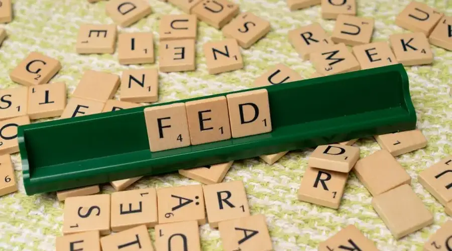Scrabble tiles spelling 'FED' on a green rack surrounded by scattered tiles on a textured surface.