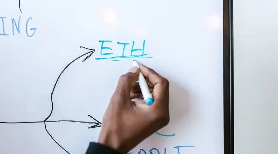 A person writes 'ETH' on a whiteboard with a blue marker, representing Ethereum.