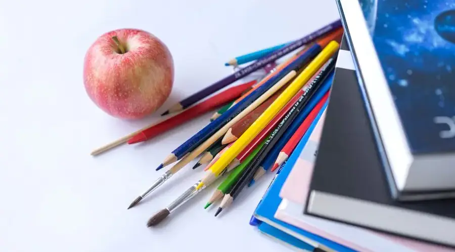 Colorful school supplies arranged with an apple on a white surface, ideal for education themes.