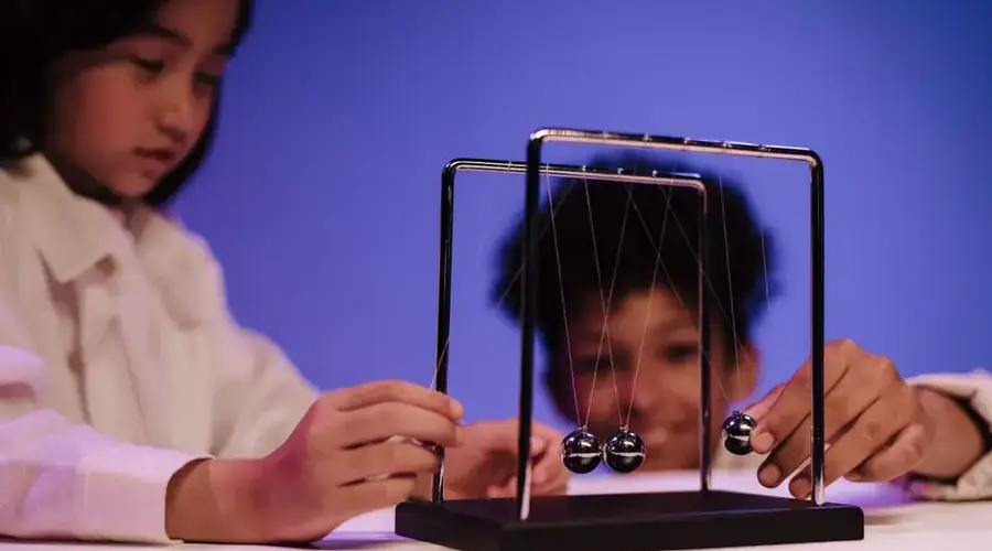 Two diverse children exploring physics concepts with a Newton's Cradle in a studio.