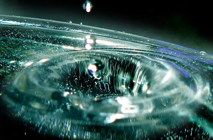 Close-up view of a water droplet creating ripples in a pool of water, capturing the moment of impact.