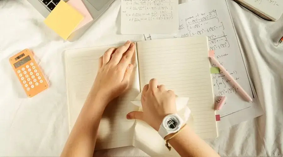 Overhead view of study materials with a laptop, calculator, and notebook on a desk.