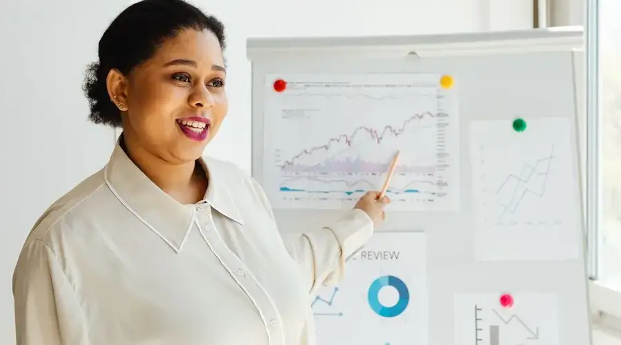 African American woman smiling while presenting financial charts on whiteboard.