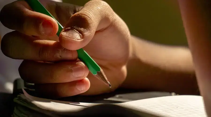 Detailed view of a hand writing with a pencil in a notebook, implying study or creativity.
