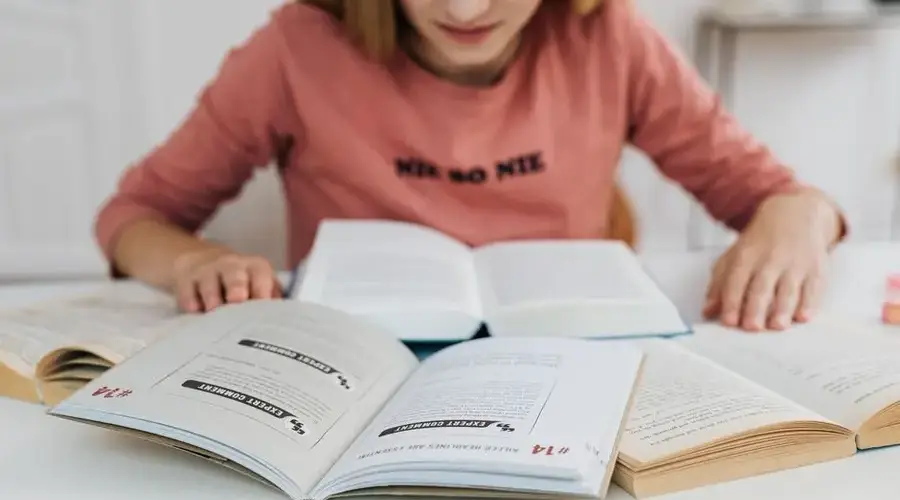 A woman in pink long sleeves studying multiple open books indoors.