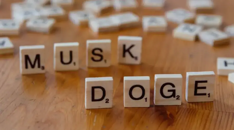 Scrabble tiles spelling 'DOGE' and 'MUSK' on a wooden table, highlighting internet culture and cryptocurrency.