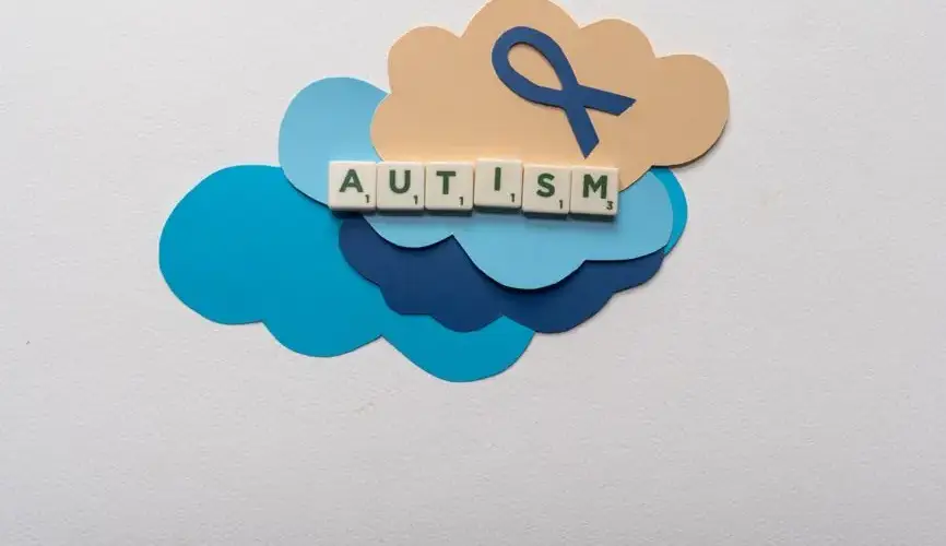 Creative representation of autism awareness using scrabble tiles on colorful clouds and ribbon.