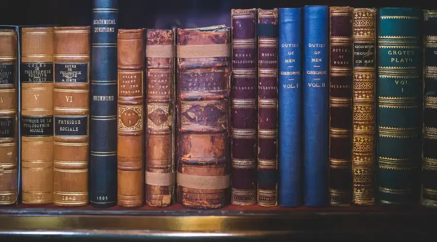 A collection of classic, leather-bound books neatly arranged on a wooden bookshelf.