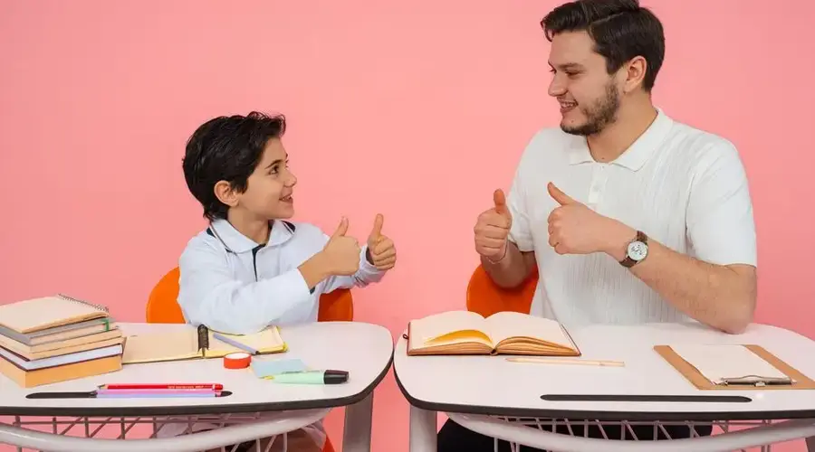 Teacher and student exchanging thumbs up at desk in a learning environment.