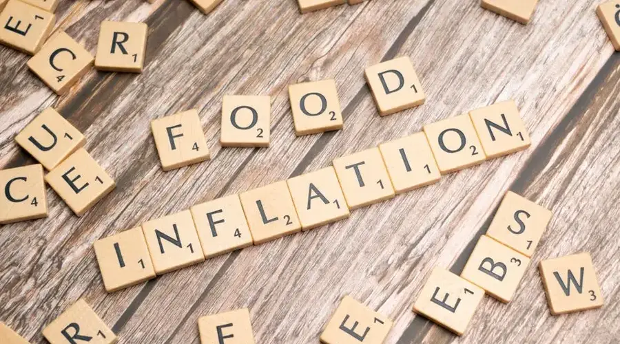 Wooden scrabble tiles arrange to spell 'Food Inflation' on a rustic wooden surface, conceptually depicting rising food prices.