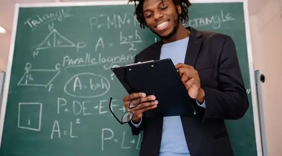 A happy teacher standing in front of a blackboard with geometric formulas, holding a clipboard.