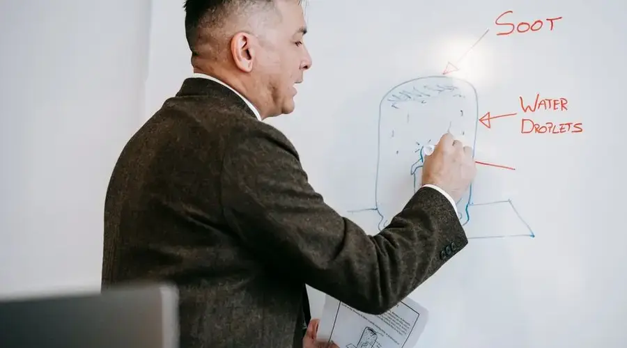 A male professional explains a diagram on a whiteboard during an educational session indoors.