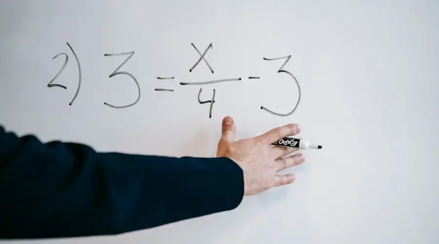 A hand writing a mathematical equation on a whiteboard with a marker.