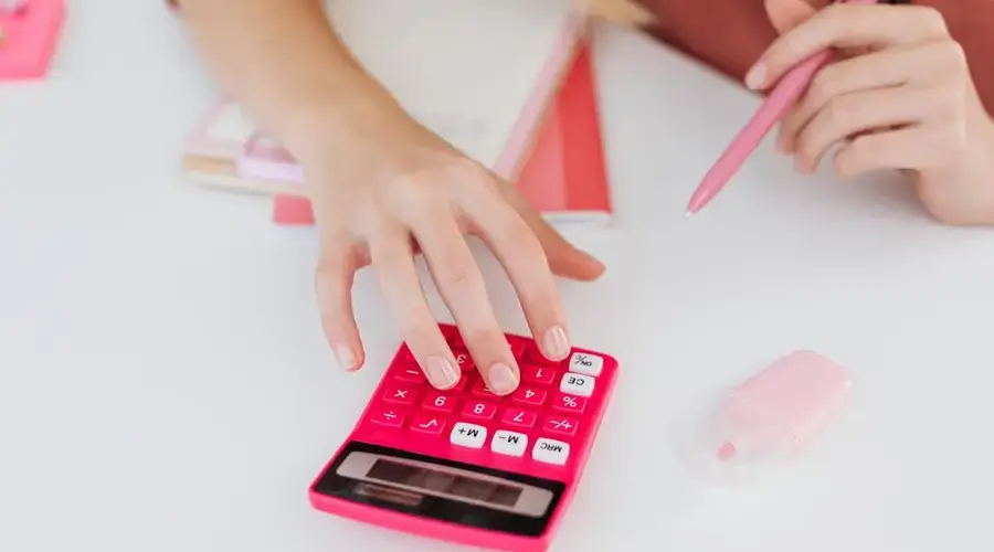 Close-up of hands using a pink calculator with notebooks and erasers, perfect for education and finance themes.