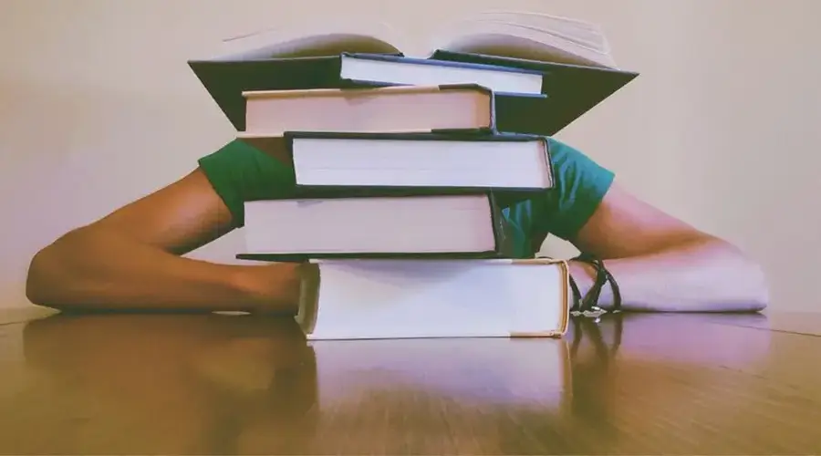 A student hidden behind a stack of books, symbolizing academic stress and study challenges.