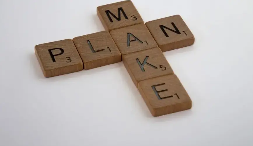Wooden Scrabble tiles forming the words 'make' and 'plan' on a clean white background.