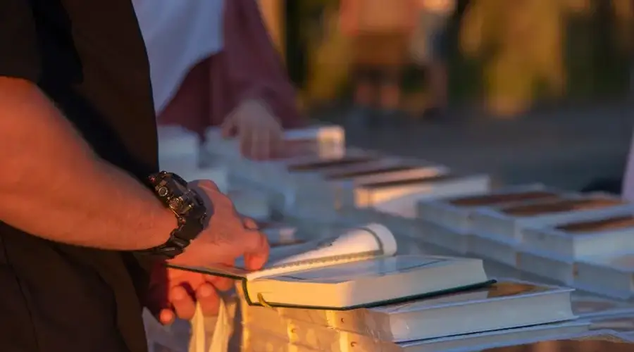 A person flipping through books at an outdoor market stall during sunset.