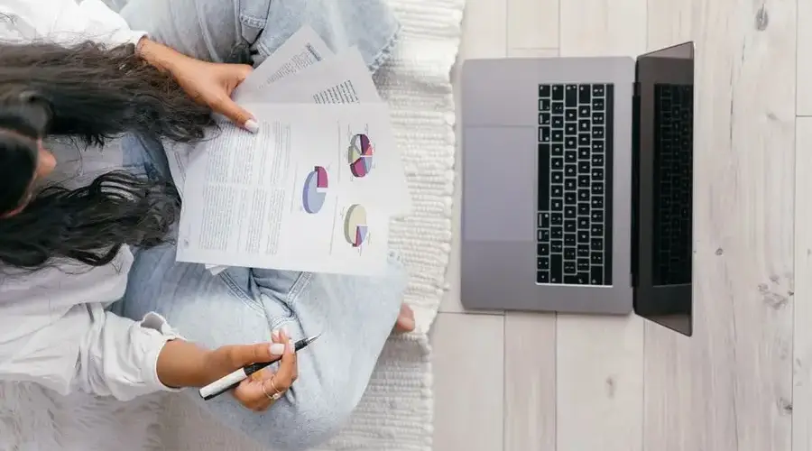 Top view of a woman studying charts on paper with a laptop, focusing on education and technology.