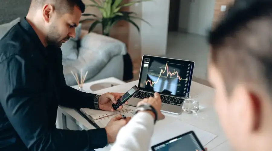 Two businessmen analyzing financial data on laptops in a modern office setting.