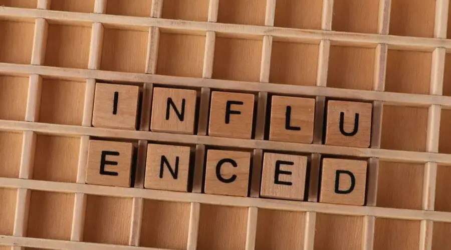 Close-up of Scrabble tiles spelling 'influenced' arranged on a wooden grid layout.