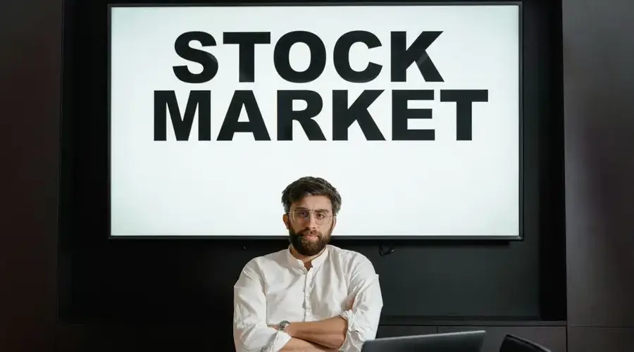 Confident businessman sitting in front of a stock market display screen in a modern office setting.