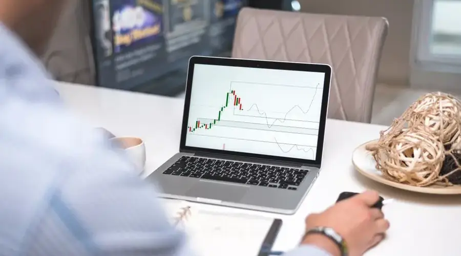 Man reviewing financial analysis on laptop in a modern office setting with focus on trading charts and data.