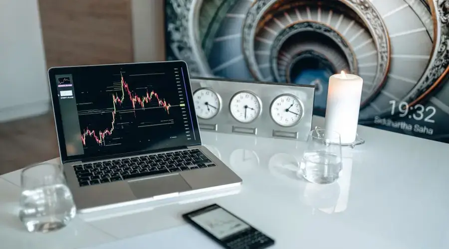 A modern desk setup featuring a laptop displaying trading charts, candles, and clocks.