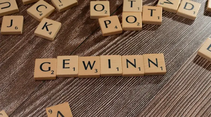 Scrabble tiles spelling 'GEWINN' on a wooden surface, symbolizing victory.