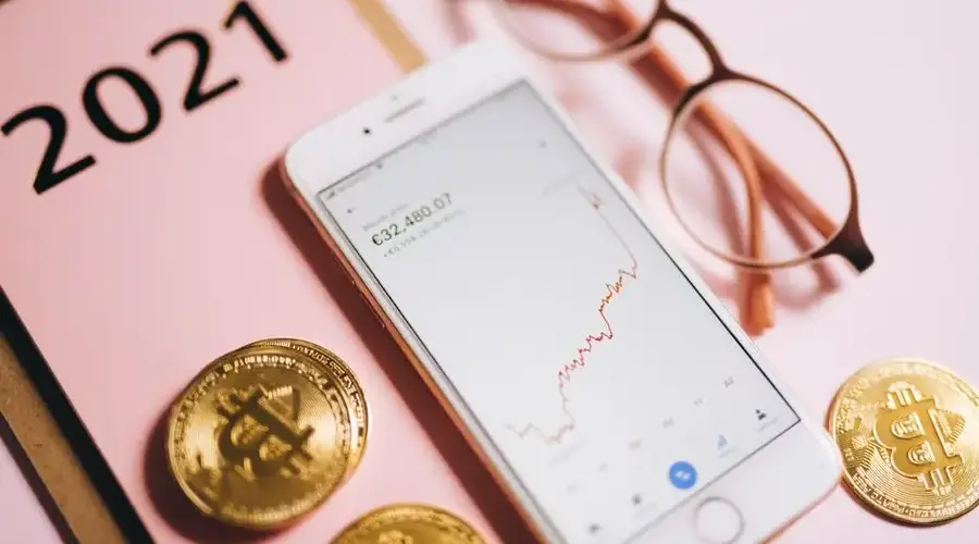 Smartphone displaying financial chart with Bitcoin coins on pink background.