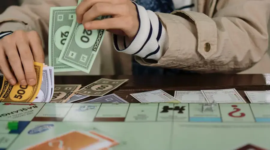 Hands counting Monopoly money during a board game session, highlighting fun and strategy.