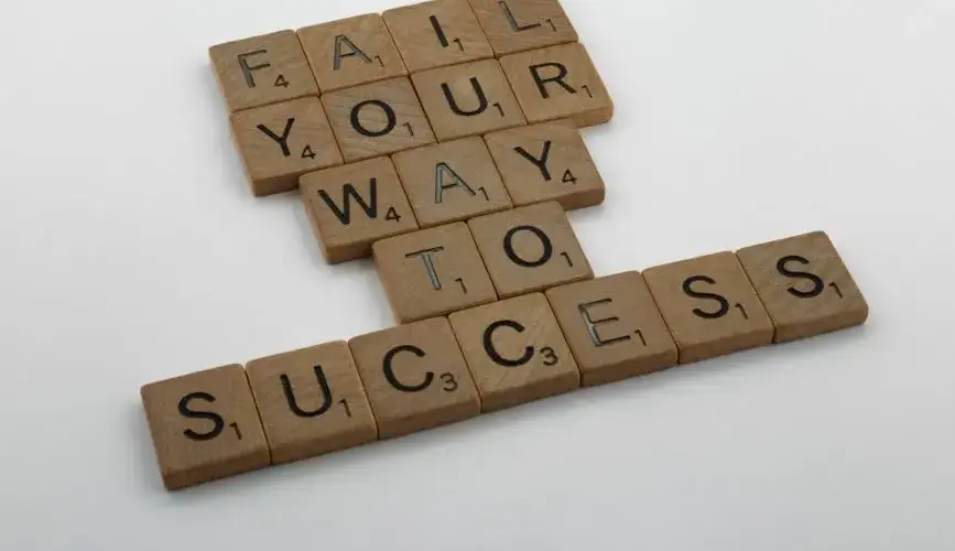 Wooden tiles spell 'Fail Your Way to Success' emphasizing perseverance.