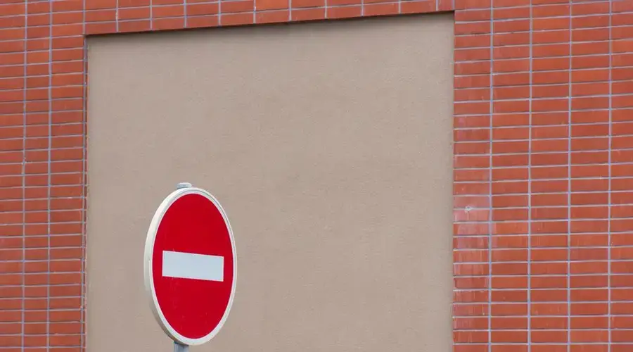 A red no entry traffic sign stands in front of a brick wall.