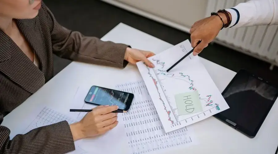 Two professionals analyzing stock market data and graphs at a desk.