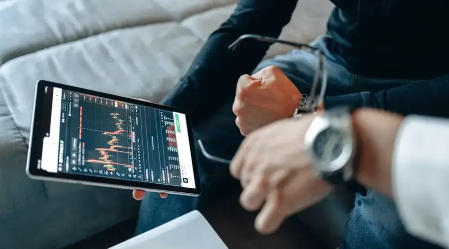 Close-up of tablet with trading charts, held by people analyzing online trades indoors.