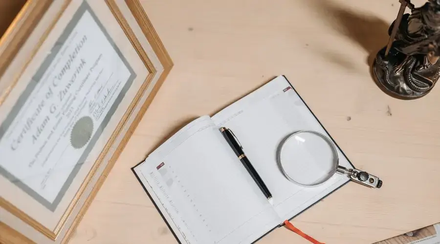 A tidy workspace featuring a certificate, open journal, magnifier, and statue on a wooden desk.