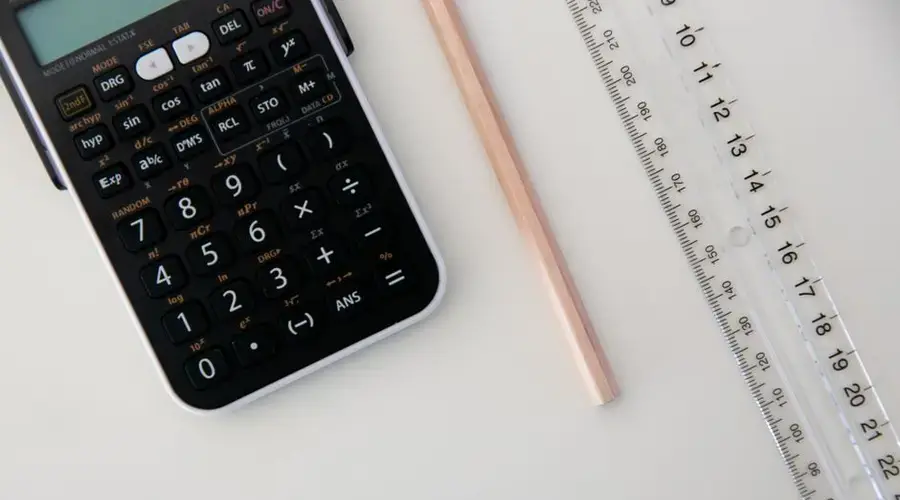 Top view of a calculator, ruler, and pencil arranged on a white surface.