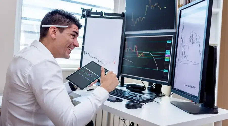 A man engaged in financial data analysis on multiple monitors in an office setting.